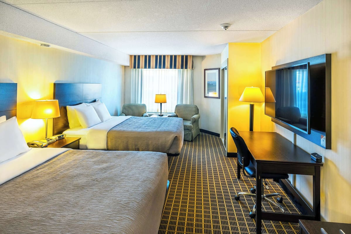 A hotel room with two beds, a desk with a TV, a chair, and a lamp.