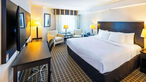 A hotel room with a large bed, a desk with a flat-screen TV, two armchairs, a small table, and two bedside lamps. - Quality Inn & Suites Garden of the Gulf (Summerside)