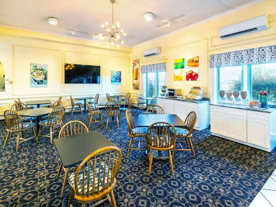 A dining area with multiple tables and chairs, a kitchen area with a window, and artwork on the walls.
