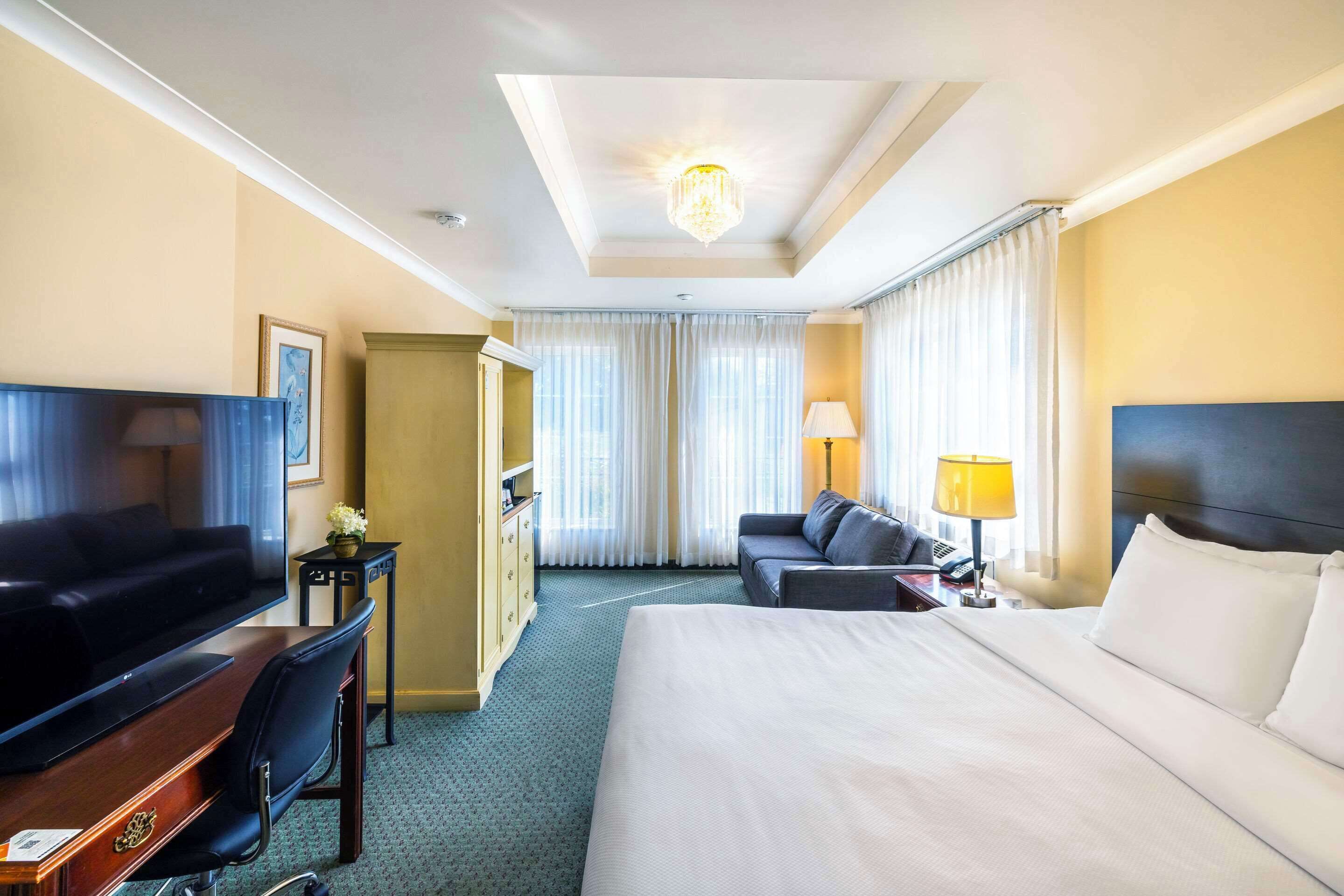 Une chambre d’hôtel avec un grand lit, une télévision, un bureau avec un ordinateur, un canapé et un lustre.