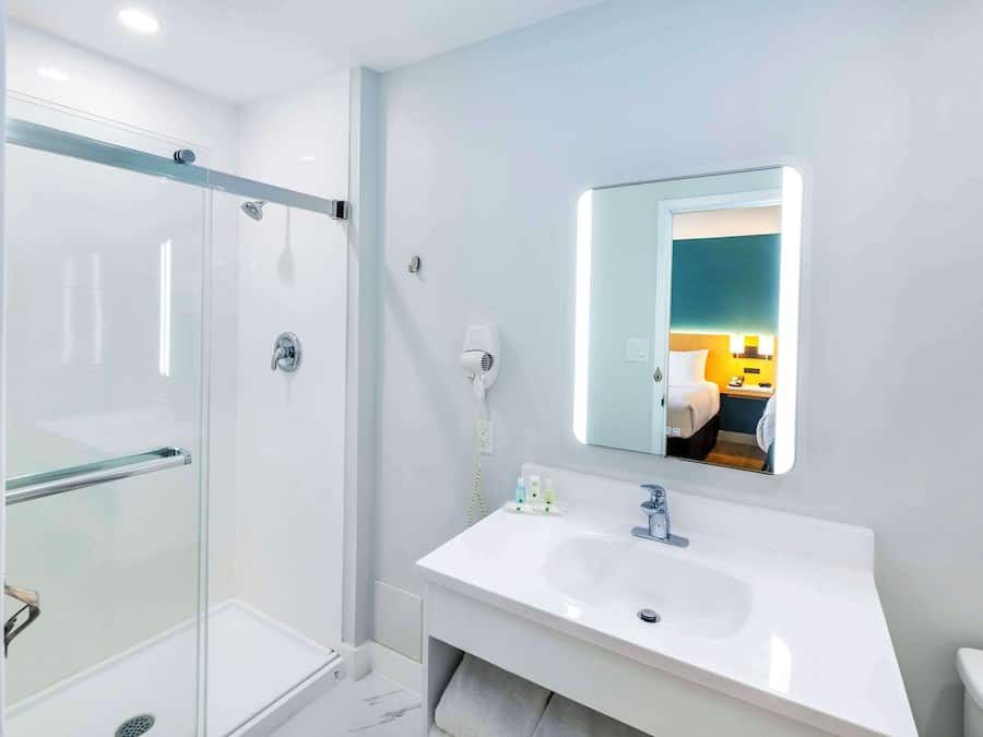 A modern bathroom with a glass-enclosed shower, a white sink with a mirror above it, and a toilet.