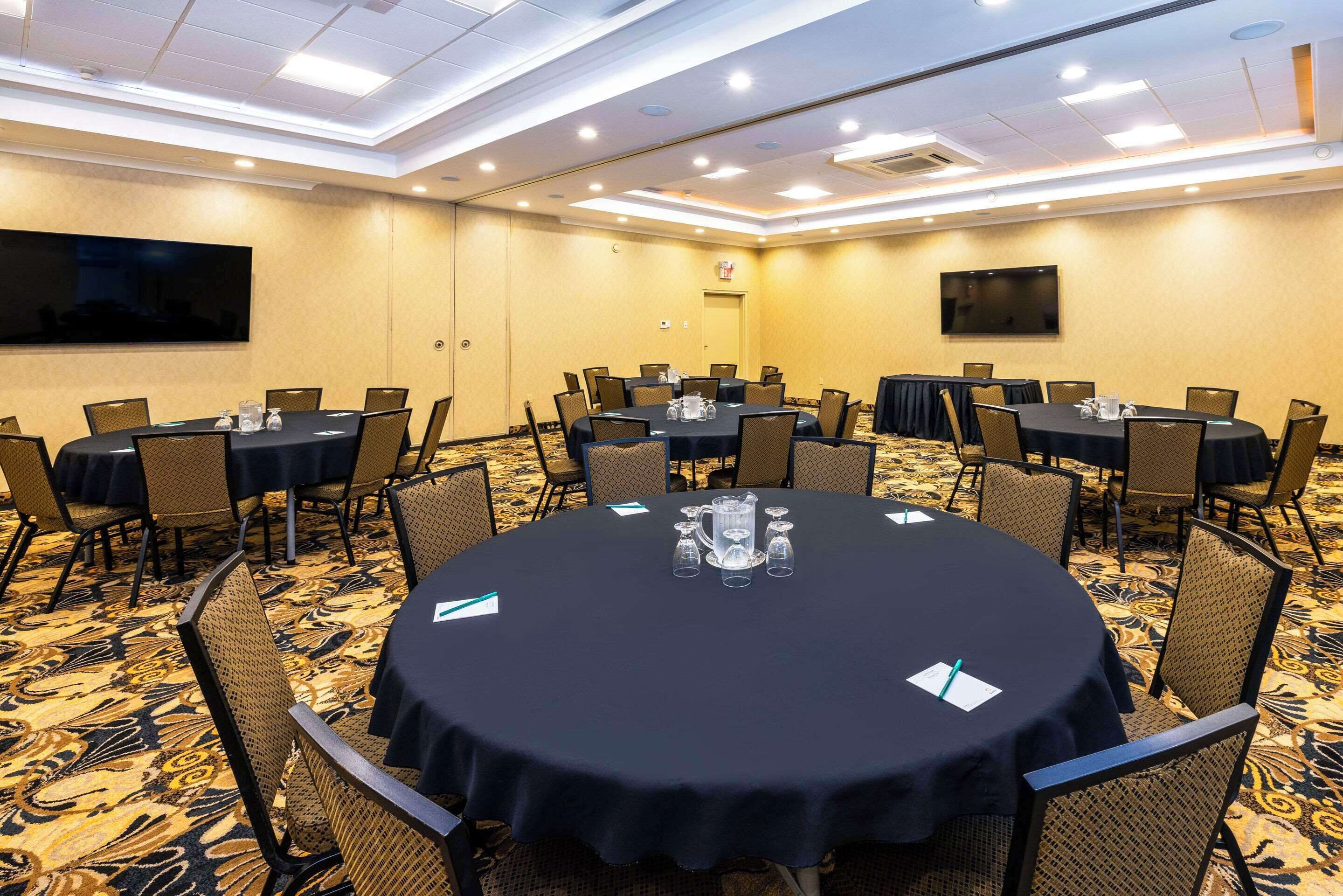 A conference room with round tables, chairs, and a large screen on the wall.