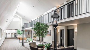 A spacious lobby with a high ceiling, a central seating area with chairs and a sofa, a large tree, and a staircase leading to an upper level. - Quality Inn & Suites Garden of the Gulf (Summerside)