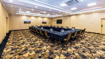 Una sala de conferencias con alfombra estampada, una larga mesa con sillas y un televisor en la pared.