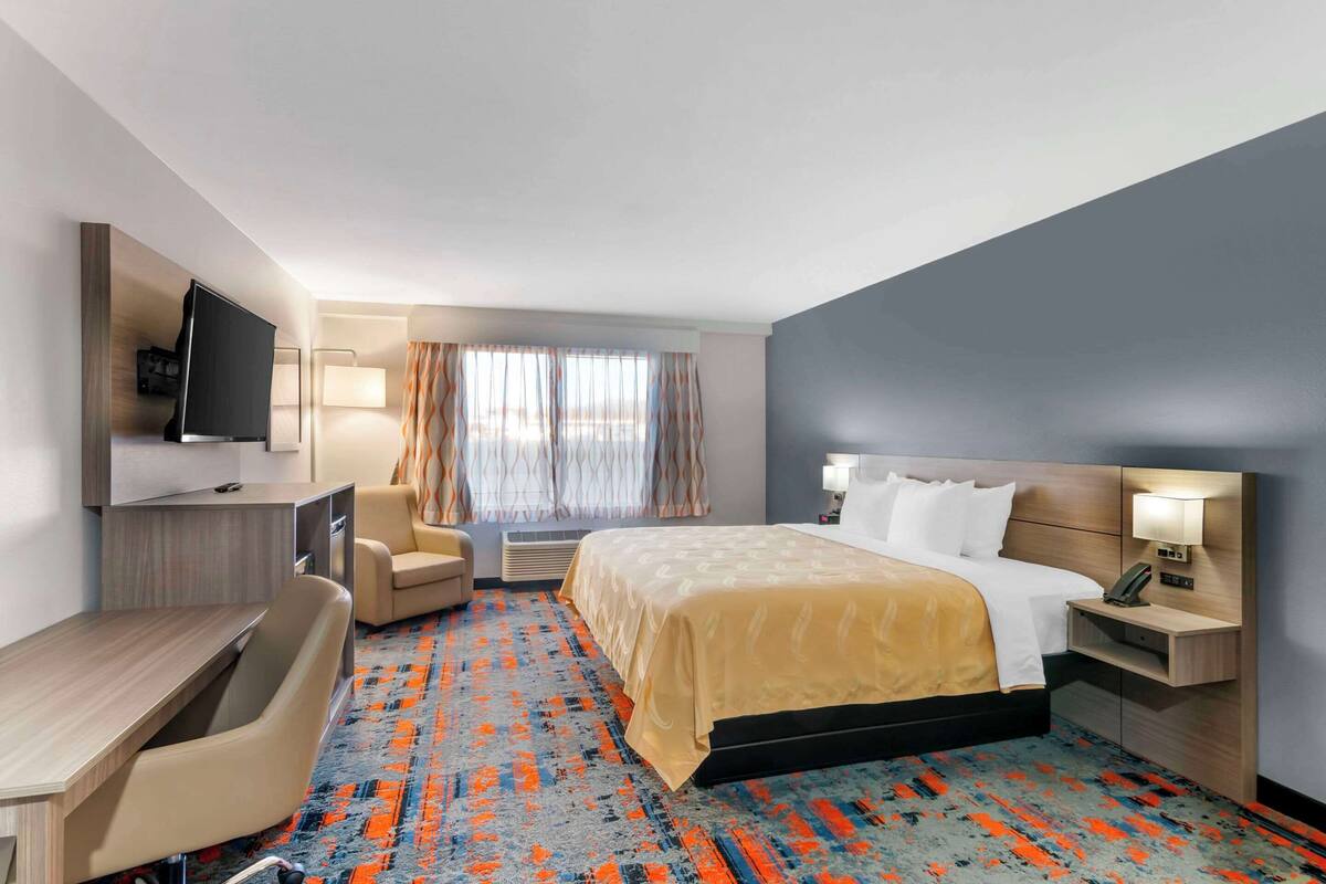 Une chambre d’hôtel équipée d’un lit, d’un bureau, d’une chaise, d’une télévision et d’une fenêtre avec des rideaux.
