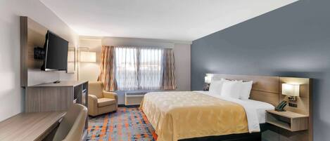 Habitación de hotel con cama, escritorio, silla, televisor y ventana con cortinas.