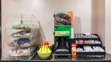 Un coin café équipé d’une machine à café, d’un panier de bananes et de divers en-cas emballés.