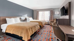 Habitación de hotel con dos camas, un escritorio, una silla, un televisor y una ventana con cortinas.