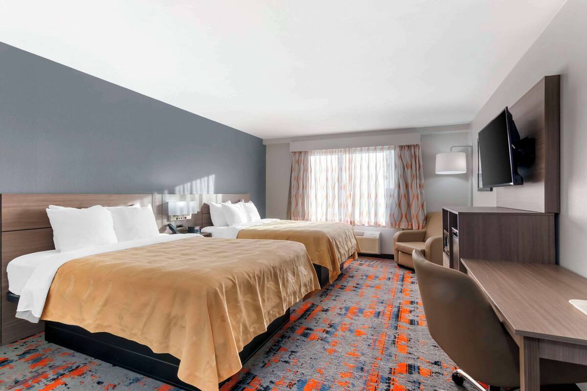 Une chambre d’hôtel avec deux lits, un bureau, une chaise, une télévision et une fenêtre avec des rideaux.