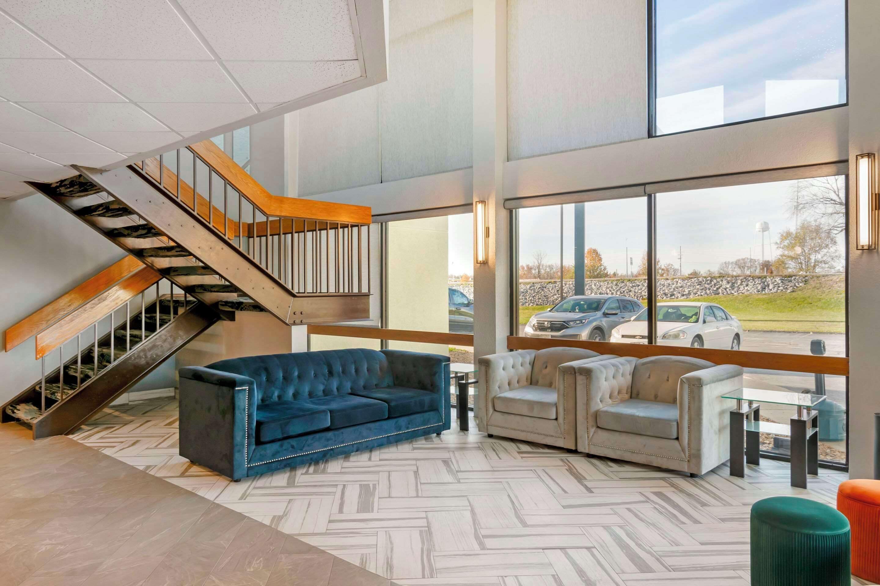 A modern interior with a herringbone floor, a staircase with wooden and metal railings, and a seating area with two sofas and a table.