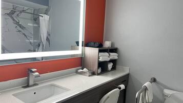 A modern bathroom with a large mirror, a sink, a toilet, and a towel rack.