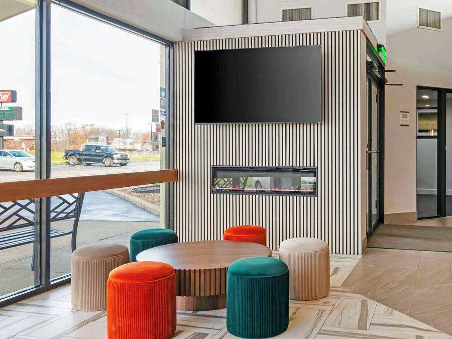 A modern interior with a large window, a flat-screen TV mounted on a wall, and a seating area with colorful stools.