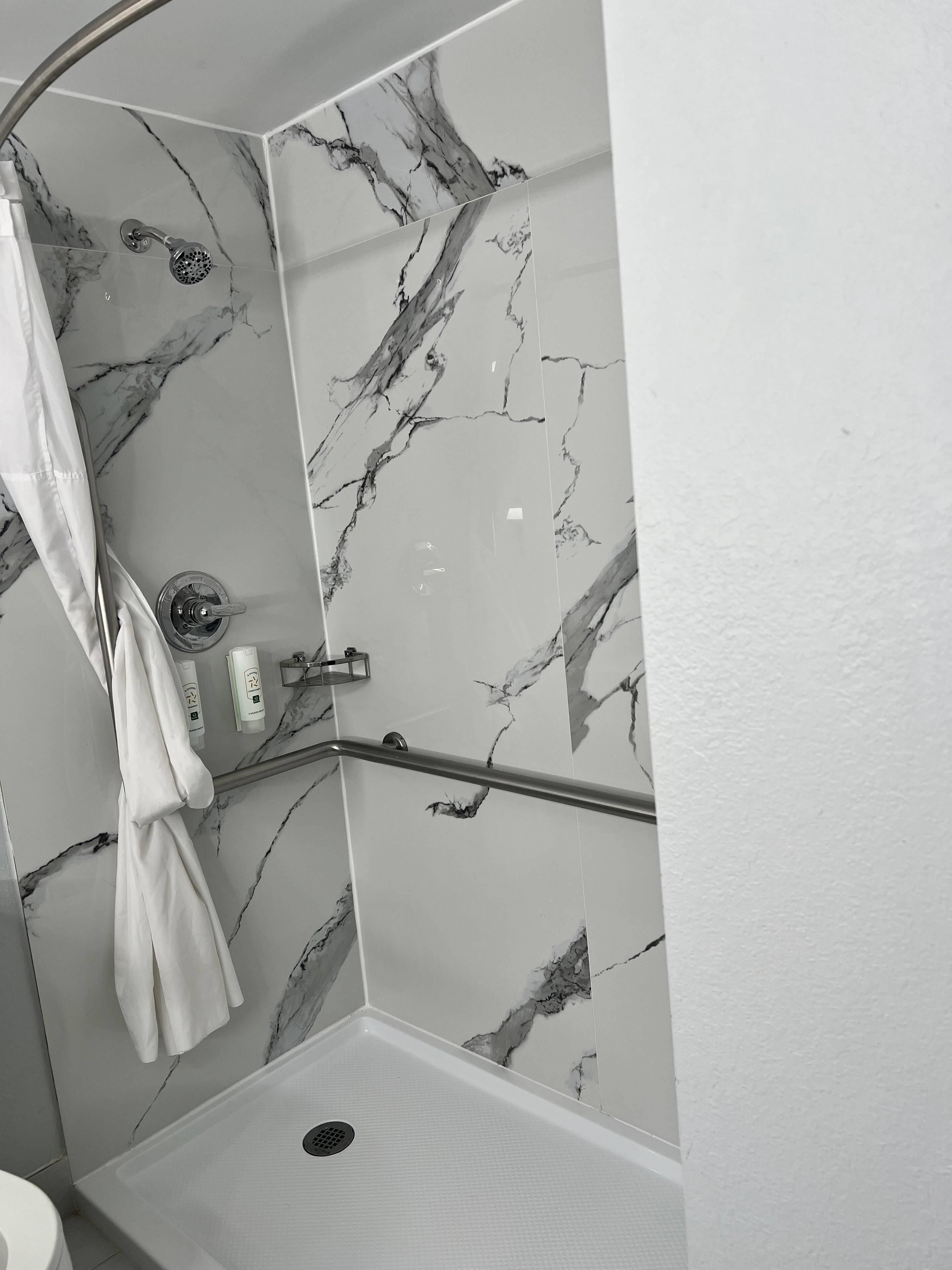 A bathroom with a shower, marble walls, a grab bar, and a towel rack.