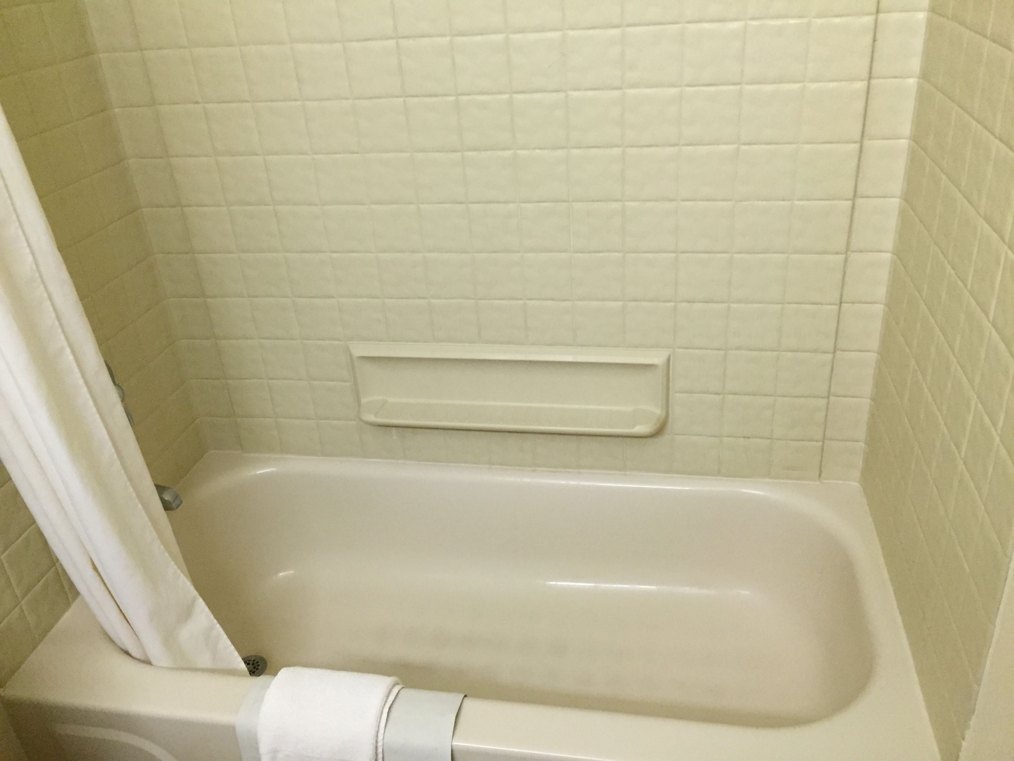 A bathroom with a bathtub, a shower curtain, and a small shelf.