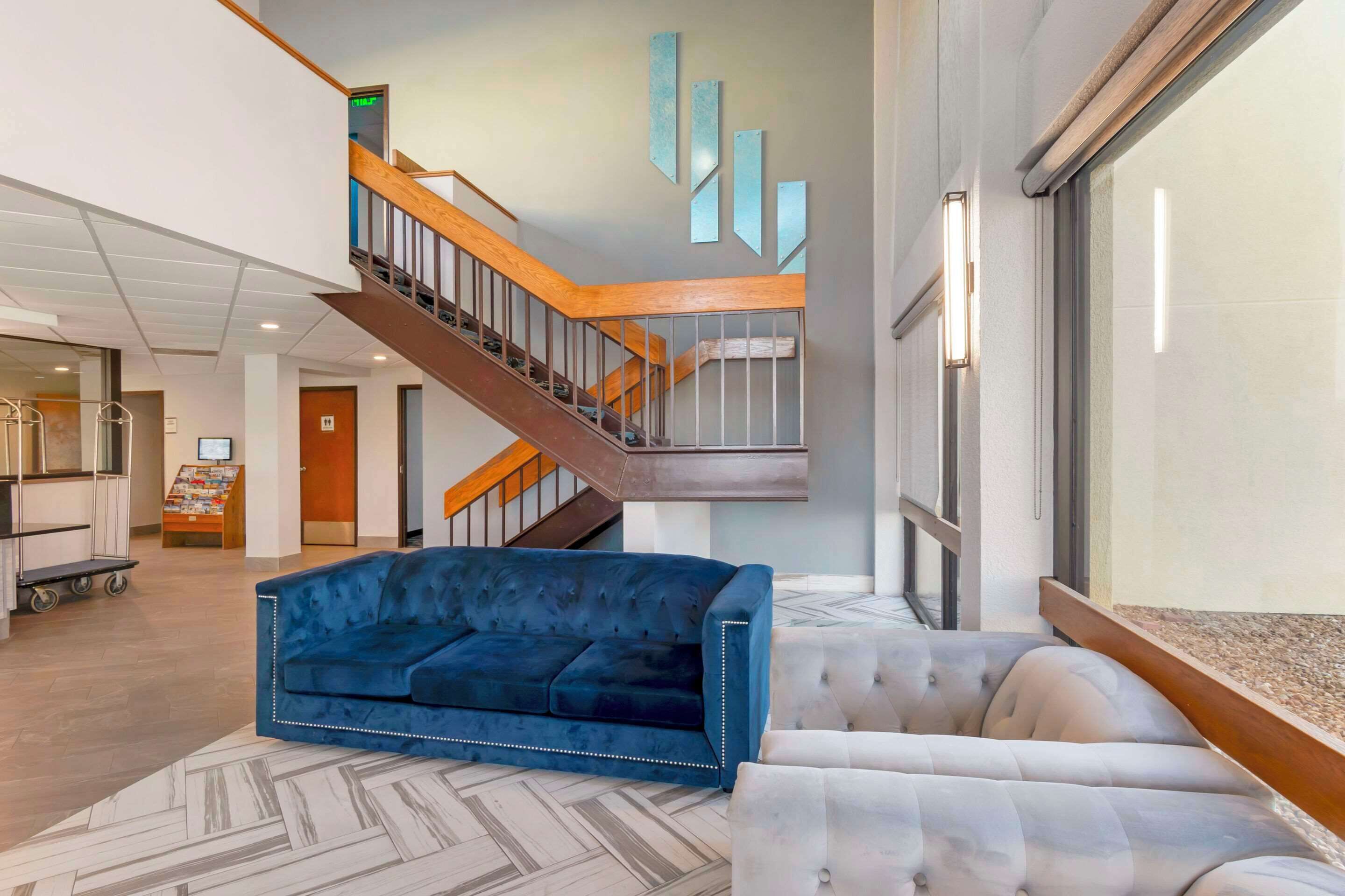 Un moderno vestíbulo de hotel con un sofá azul, una escalera y un ventanal amplio.