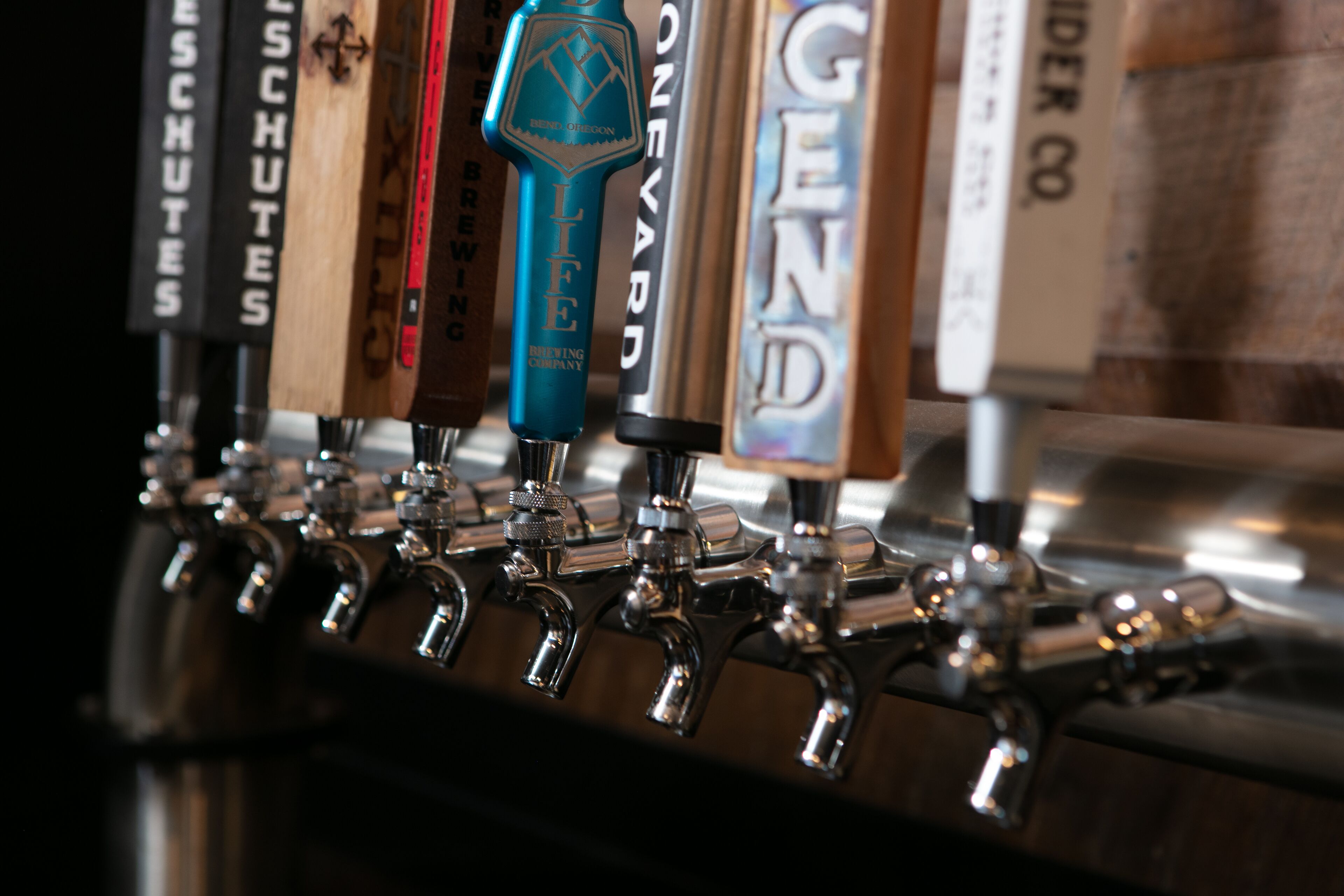A row of beer taps with labels such as "Life Brewing Company" and "Ginger Beer".