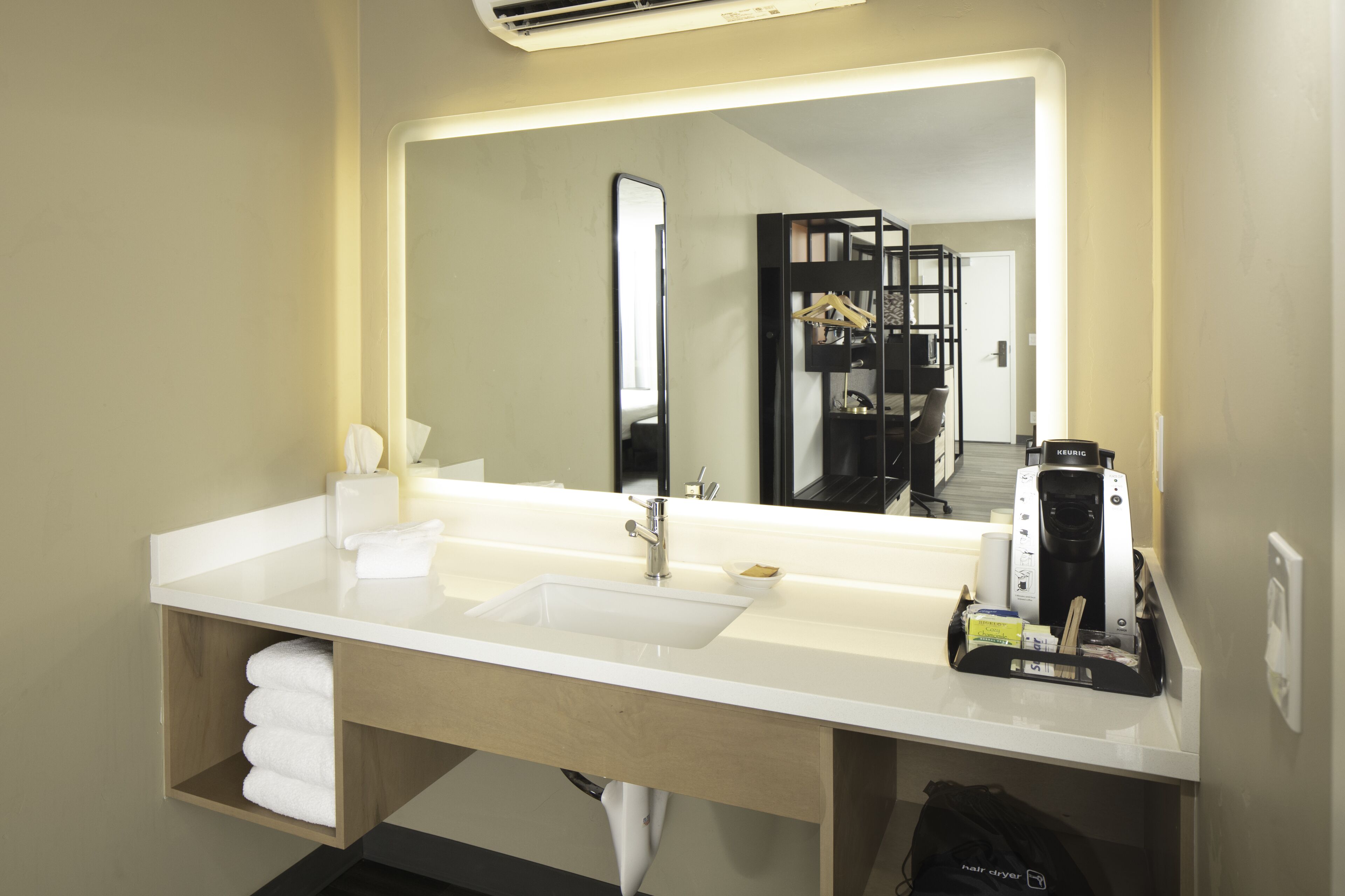A modern bathroom with a white sink, a large mirror, and a coffee machine.