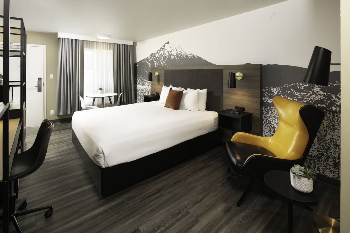 Quarto de hotel com uma cama, uma escrivaninha, uma cadeira e um mural com tema de montanhas na parede.