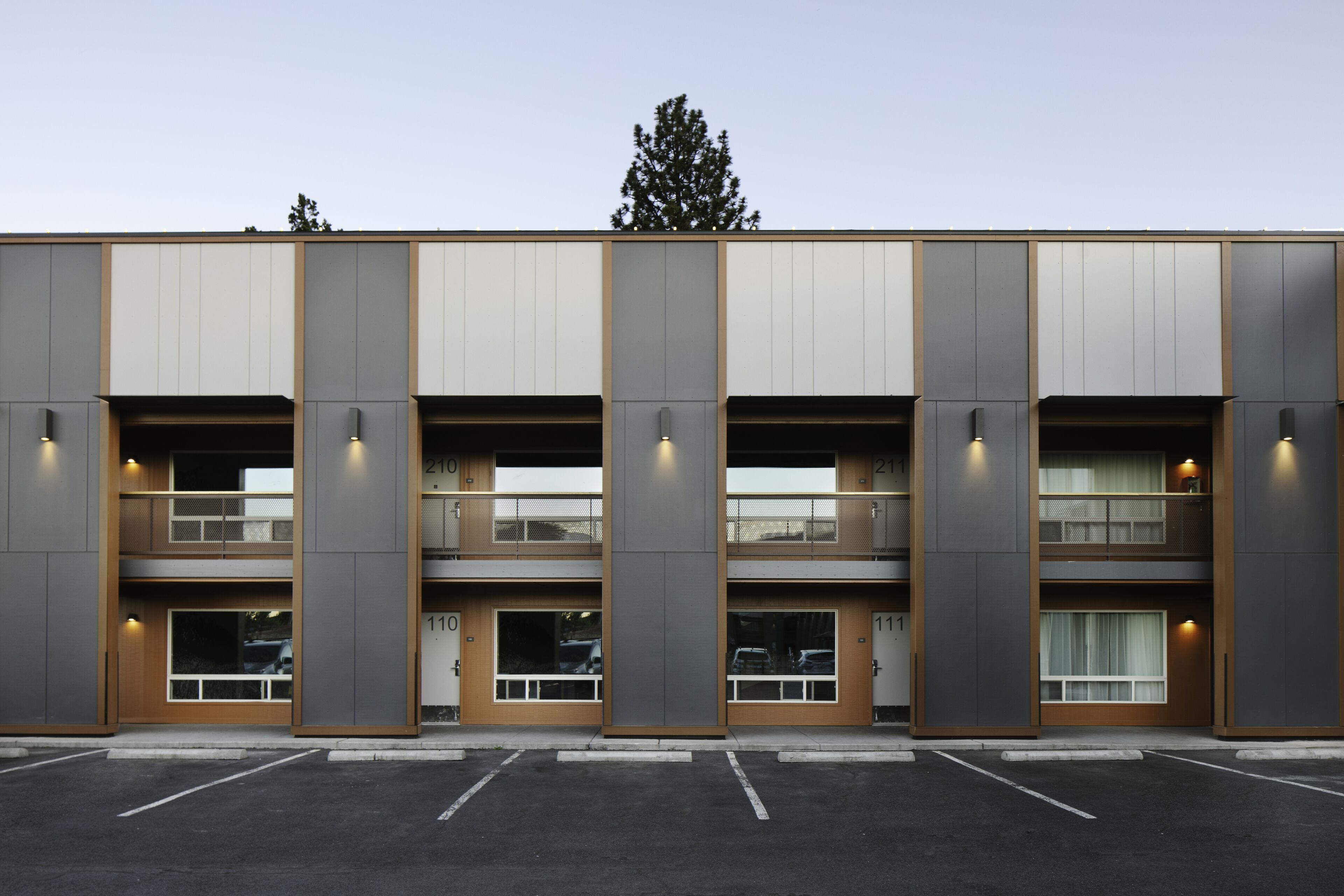 A modern building with a symmetrical facade, multiple balconies, and a parking lot in front.