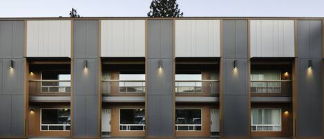 A modern building with a symmetrical facade, multiple balconies, and a parking lot in front.