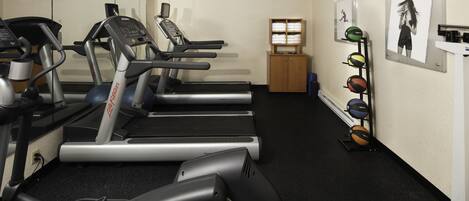 A gym with treadmills, a wall-mounted rack of exercise balls, and a wooden cabinet with towels.