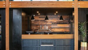 Un comptoir d’accueil avec un plateau en bois et une pancarte « Bienvenue », entouré d’étagères remplies de bouteilles et de verres, et éclairé par des suspensions.
