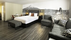 Une chambre d’hôtel moderne avec un grand lit, un canapé gris, une petite table et une chaise.