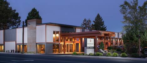 A modern hotel with a prominent entrance, a covered outdoor area, and a well-lit facade.