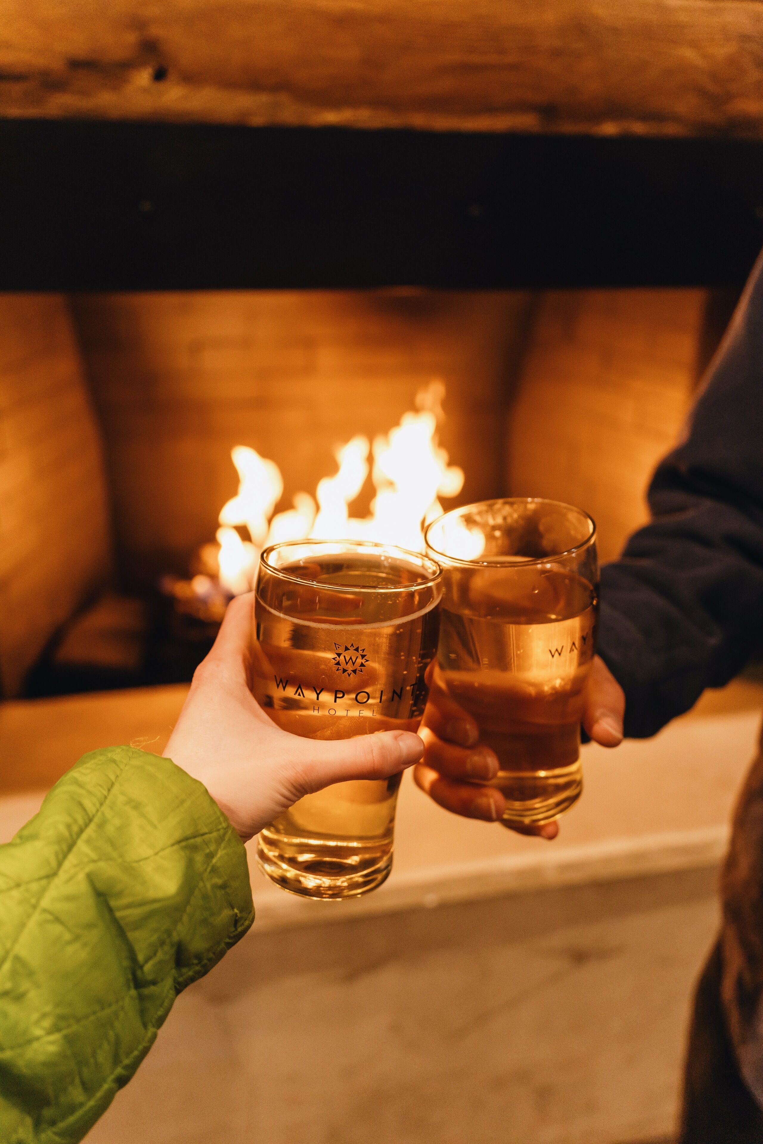 Two people holding glasses with a lit fireplace in the background.