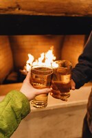 Two people holding glasses with a lit fireplace in the background.