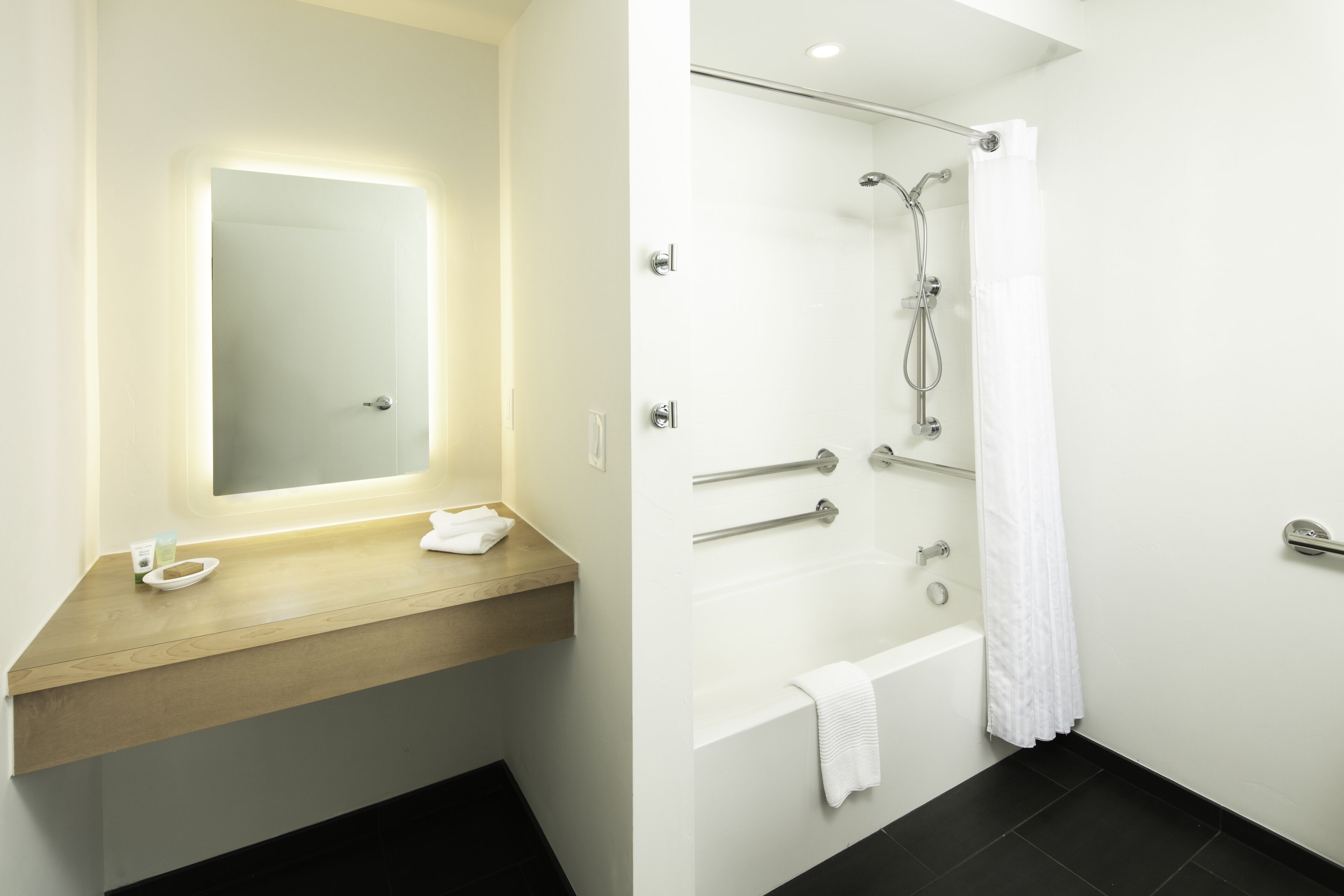 A modern bathroom with a wooden vanity, a large mirror, a shower with a glass door, and a white towel hanging on the wall.