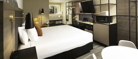 Una habitación de hotel moderna con una cama grande, un escritorio con computadora, televisor y zona de estar.