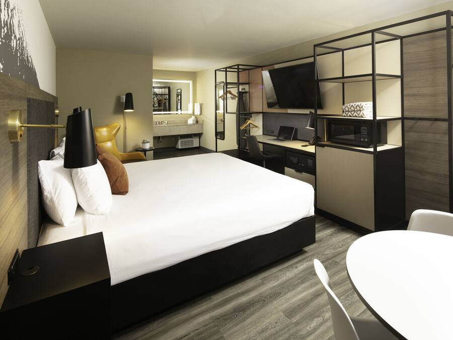A modern hotel room with a large bed, a desk with a computer, a TV, and a seating area.