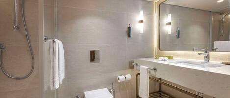 A modern bathroom with a glass-enclosed shower, a toilet, a sink with a towel rack, and a mirror with integrated lighting.