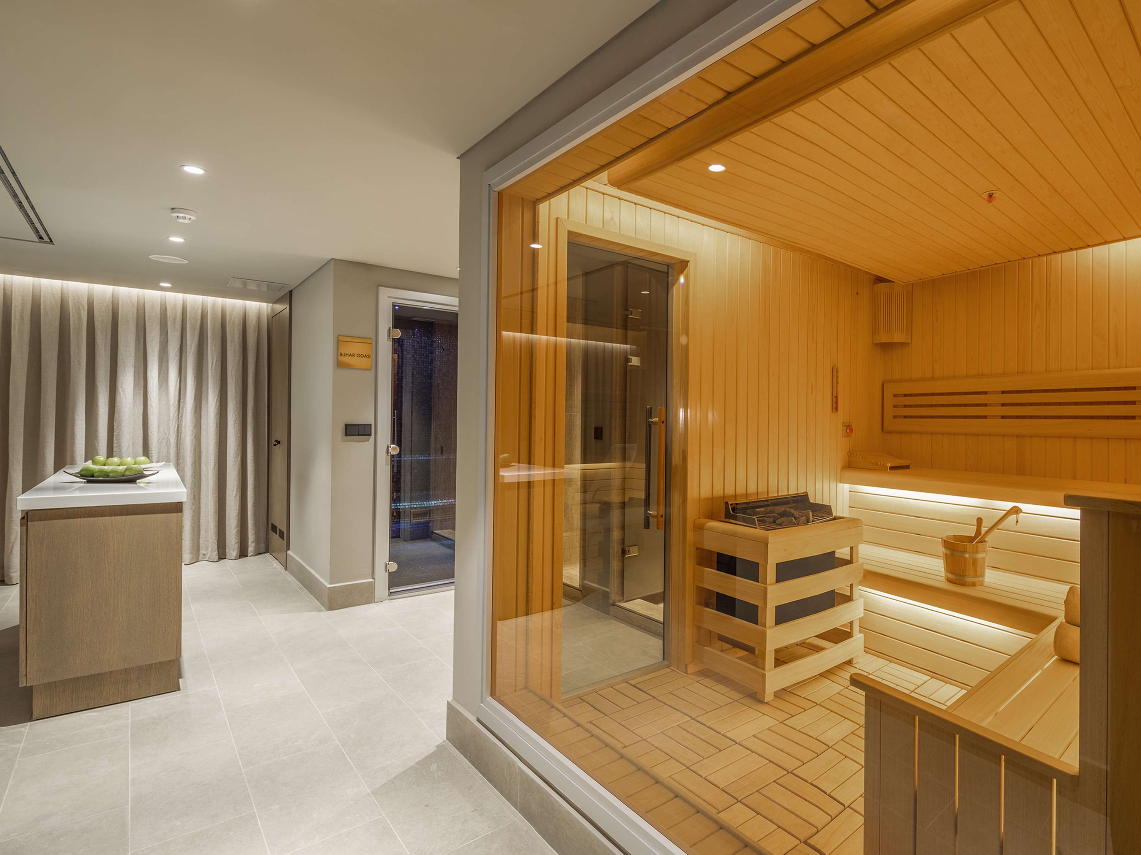 Une chambre d’hôtel moderne dotée d’un sauna en bois, d’une douche en verre et d’une petite table en bois sur laquelle se trouve un bol.