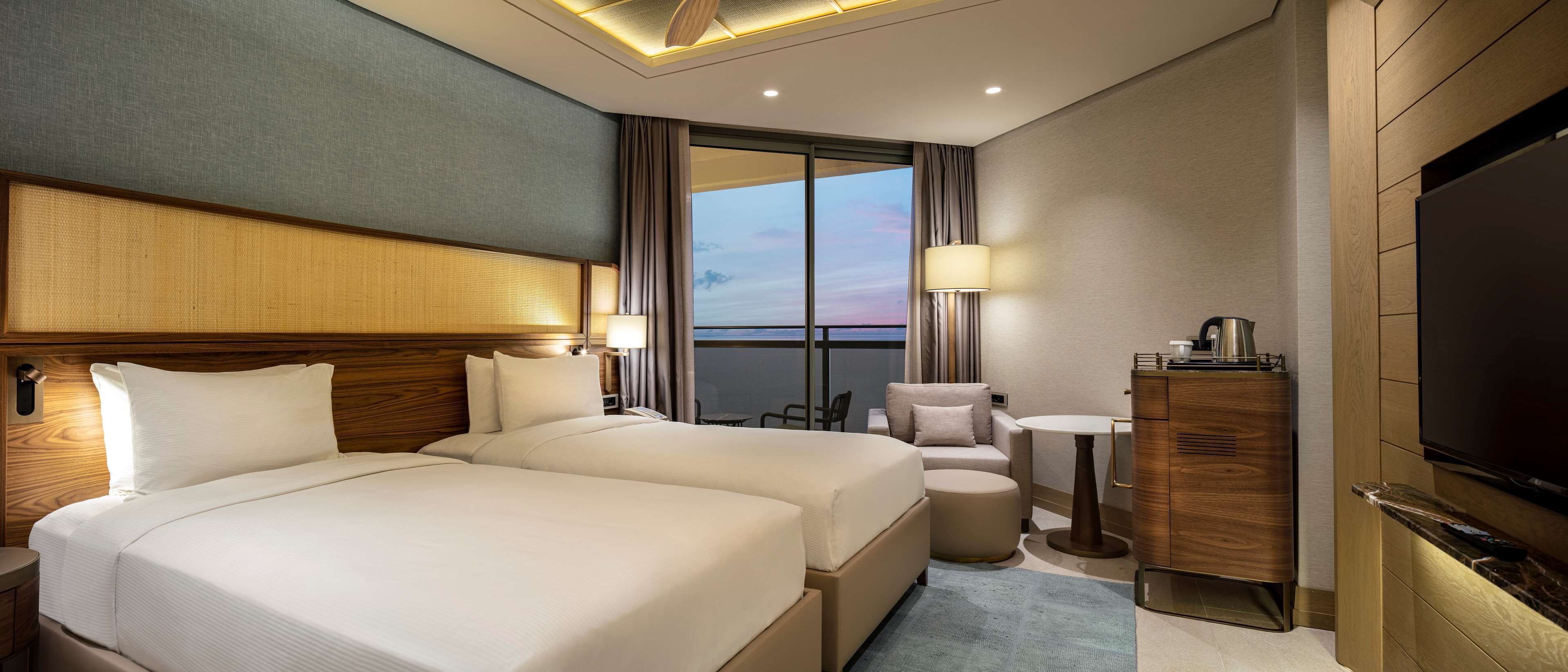 Ein Hotelzimmer mit zwei Betten, einem Fernseher, einem Schreibtisch und Blick auf die Stadt.