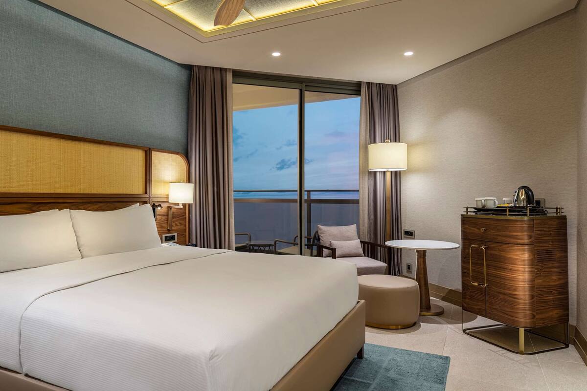 Quarto de hotel com cama grande, escrivaninha, televisão, mesa pequena e vista para o mar.