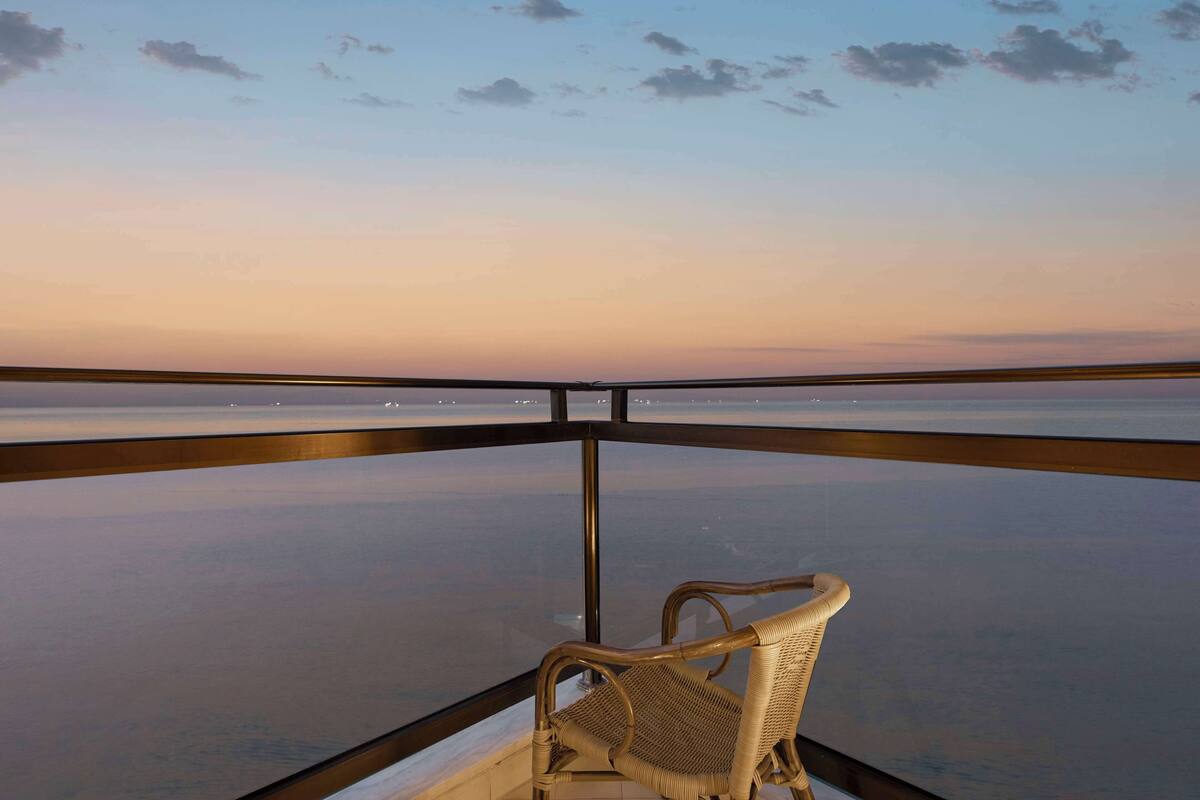 Varanda com cadeira de vime com vista para um corpo d'água calmo ao pôr do sol.