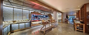A modern restaurant with a sushi bar, a buffet with various dishes, and a seating area with tables and chairs. - Mersin HiltonSA (Mersin)