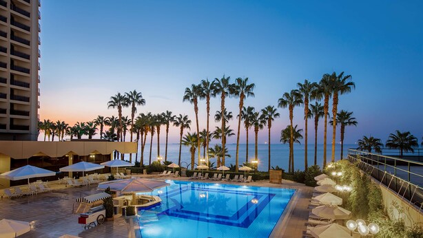 A pool area with lounge chairs and umbrellas, surrounded by palm trees and overlooking a body of water. - Mersin HiltonSA (Mersin)