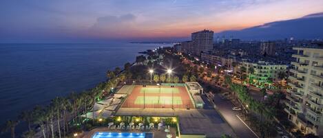 Un resort con piscina, canchas de tenis y vistas al mar y al horizonte de la ciudad.