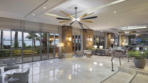 A spacious lobby with a high ceiling, modern lighting fixtures, and a view of the sea through large windows. - Mersin HiltonSA (Mersin)