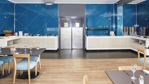 A modern dining area with a central island, wooden chairs, and a glass-top table. - ibis Styles Geraldton (Tarcoola Beach)