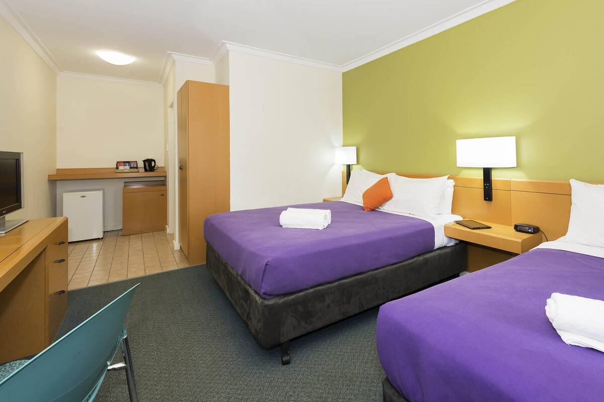 Habitación de hotel con dos camas, un escritorio, una kitchenette pequeña y un televisor.