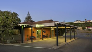 A building with a sign reading 'ibis Styles Geraldton' with a covered outdoor seating area and a paved entrance. - ibis Styles Geraldton (Tarcoola Beach)