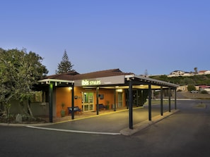 Un bâtiment portant une enseigne indiquant « ibis Styles Geraldton », avec un espace extérieur abrité pour s’asseoir et une entrée dallée.