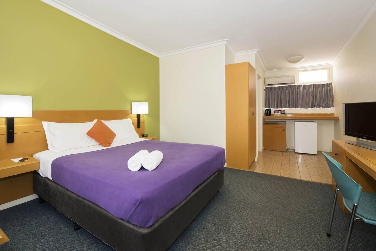 Una habitación de hotel con cama, escritorio, televisor y kitchenette.