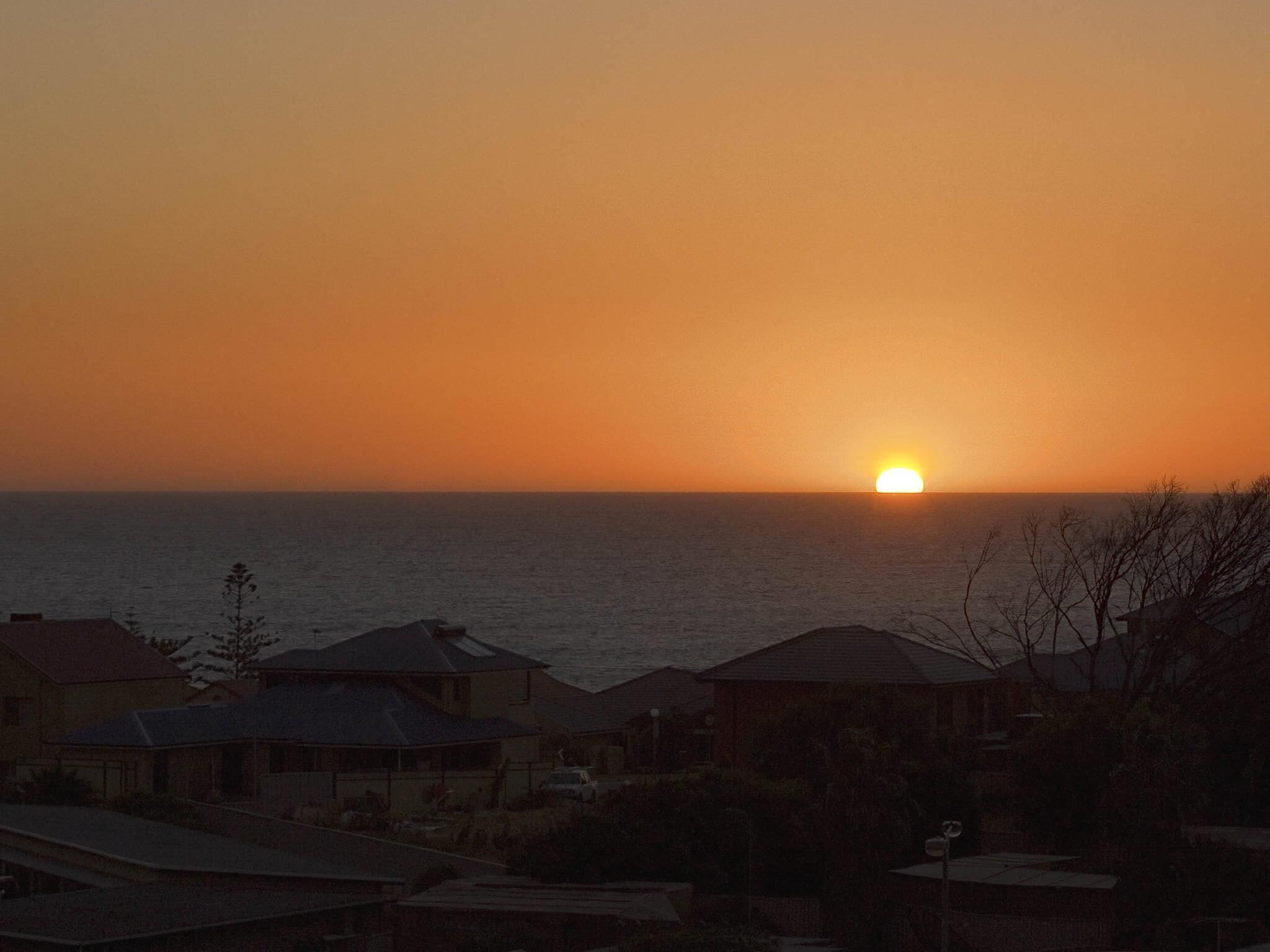 A sunset over the ocean with houses in the foreground.