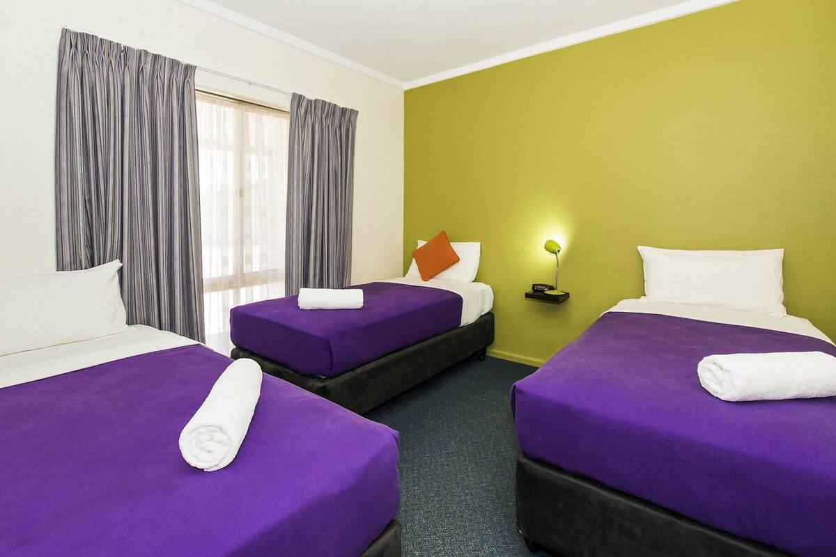 Una habitación de hotel con dos camas, una mesita de noche, una lámpara y una ventana con cortinas.