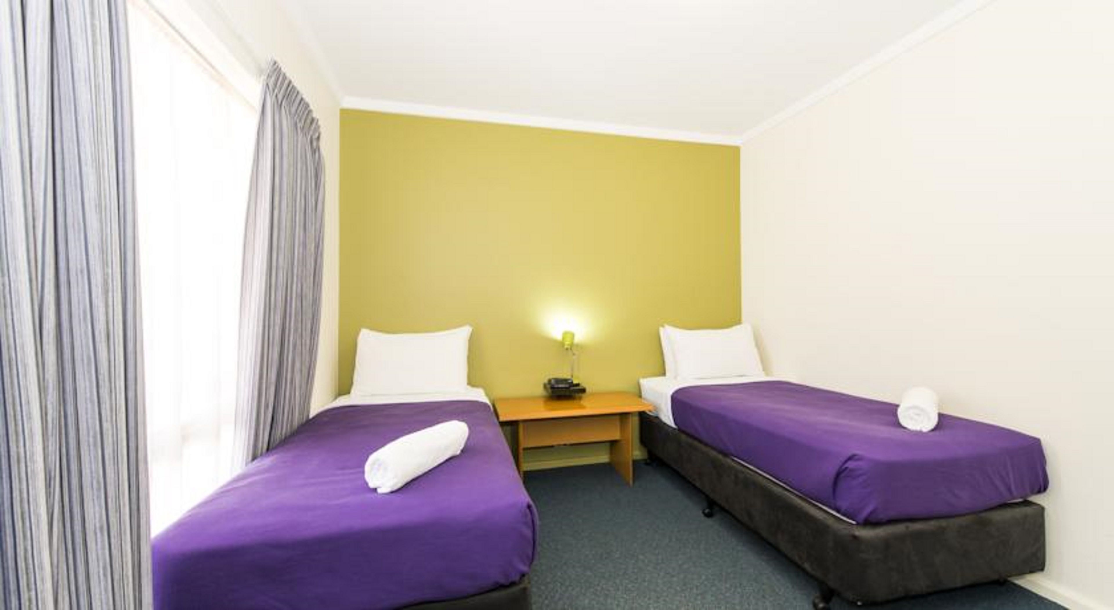 A small hotel room with two beds, a nightstand, and a lamp.